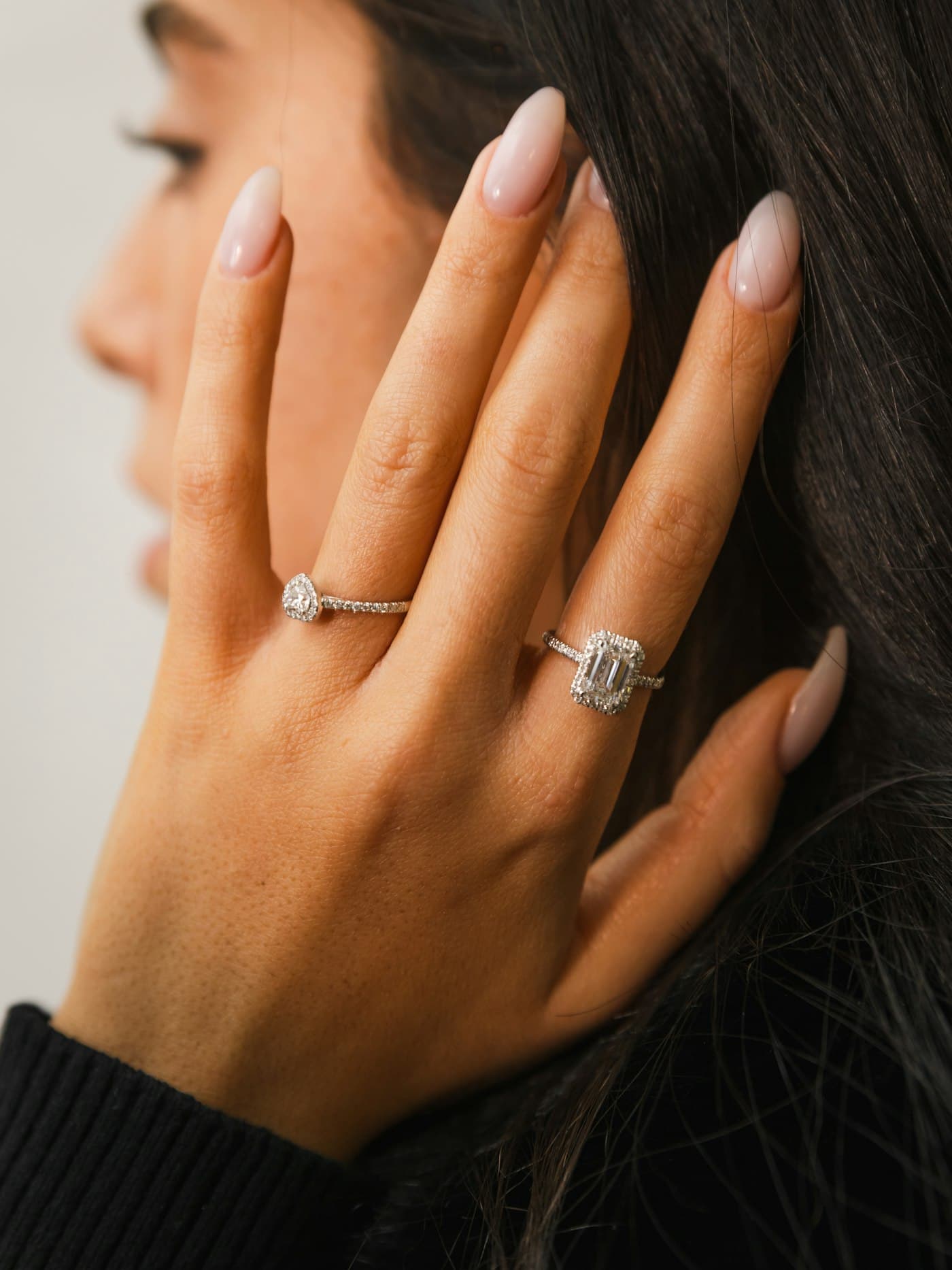 A woman's hand wearing diamond rings, raised to her face
