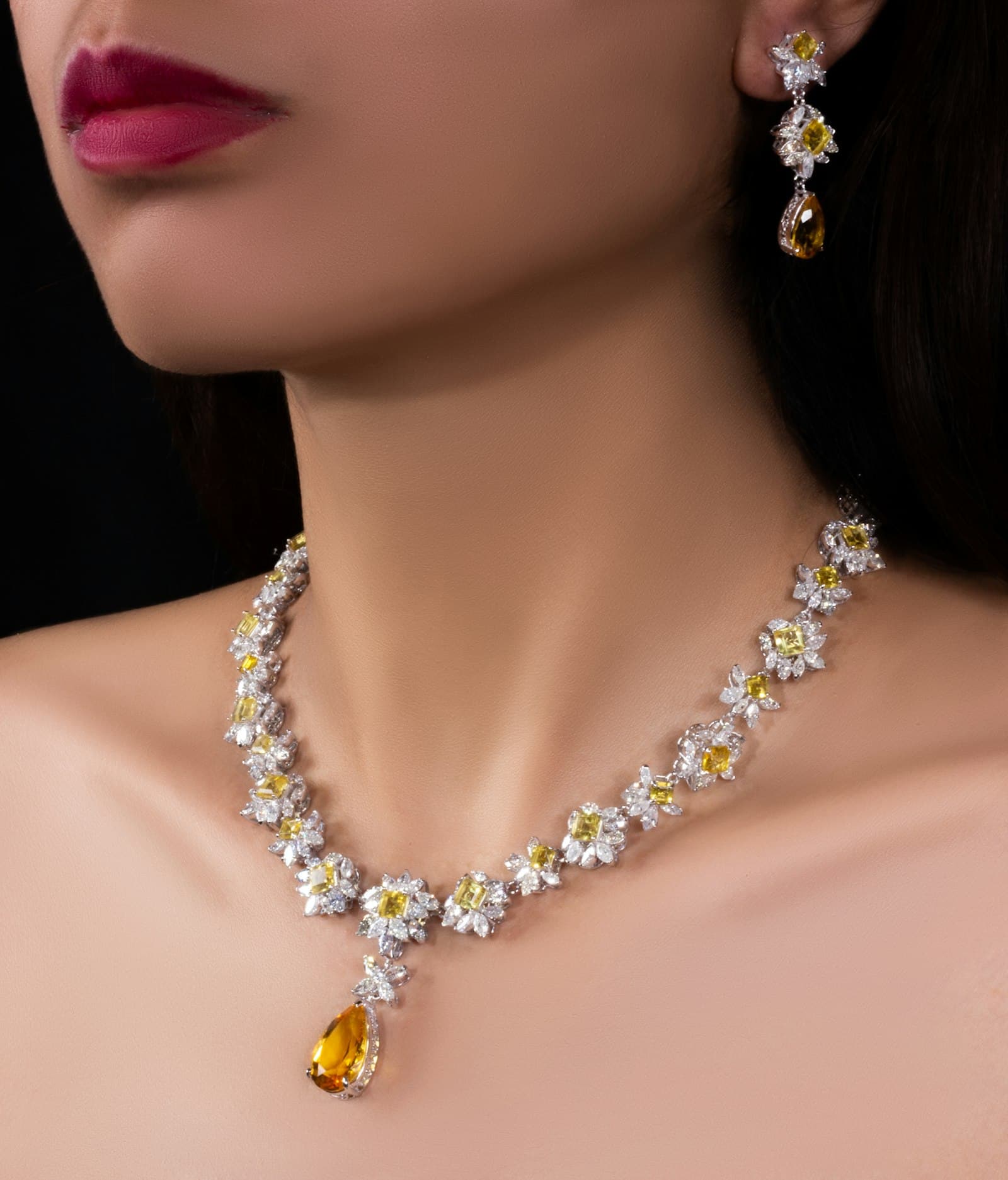 Woman wearing a diamond necklace and drop earrings against a dark background