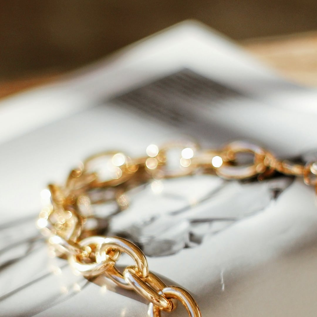 Close-up detail — chunky gold chain link bracelet resting on an open magazine
