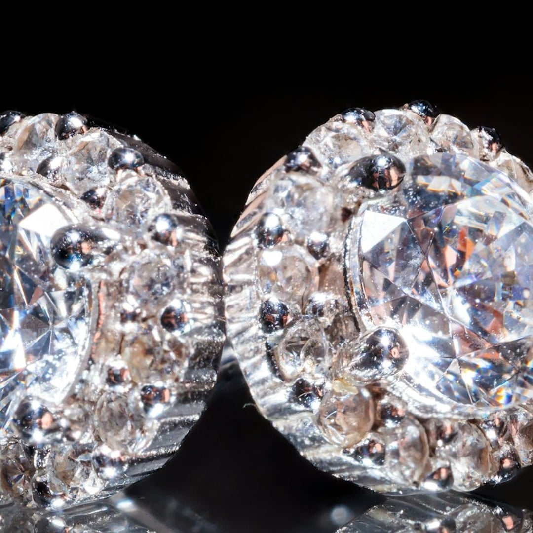 Close-up detail — pair of round diamond halo stud earrings reflected on a black surface