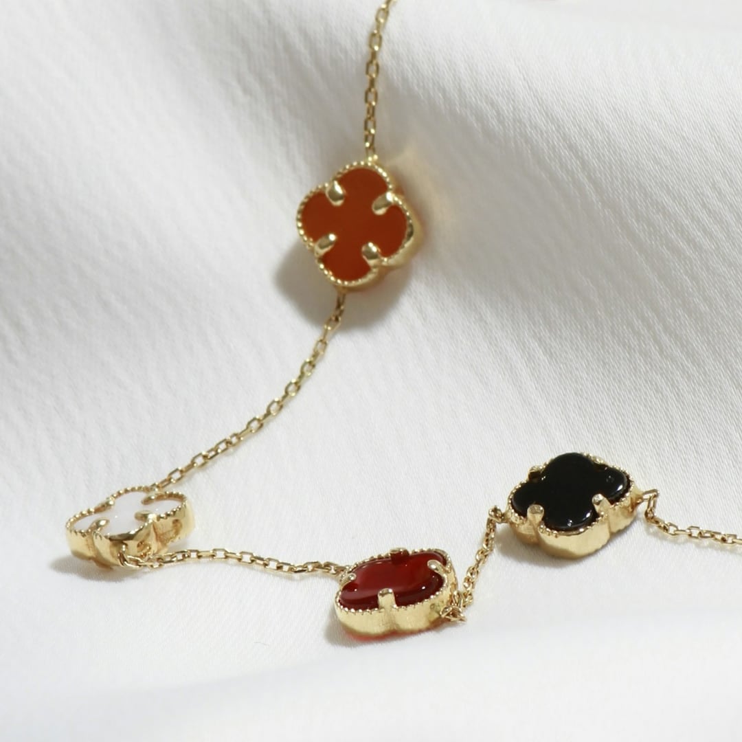 Close-up detail — delicate gold chain bracelet with bezel-set coloured gemstones on white fabric