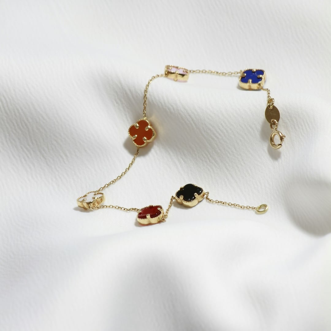 Delicate gold chain bracelet with bezel-set coloured gemstones on white fabric