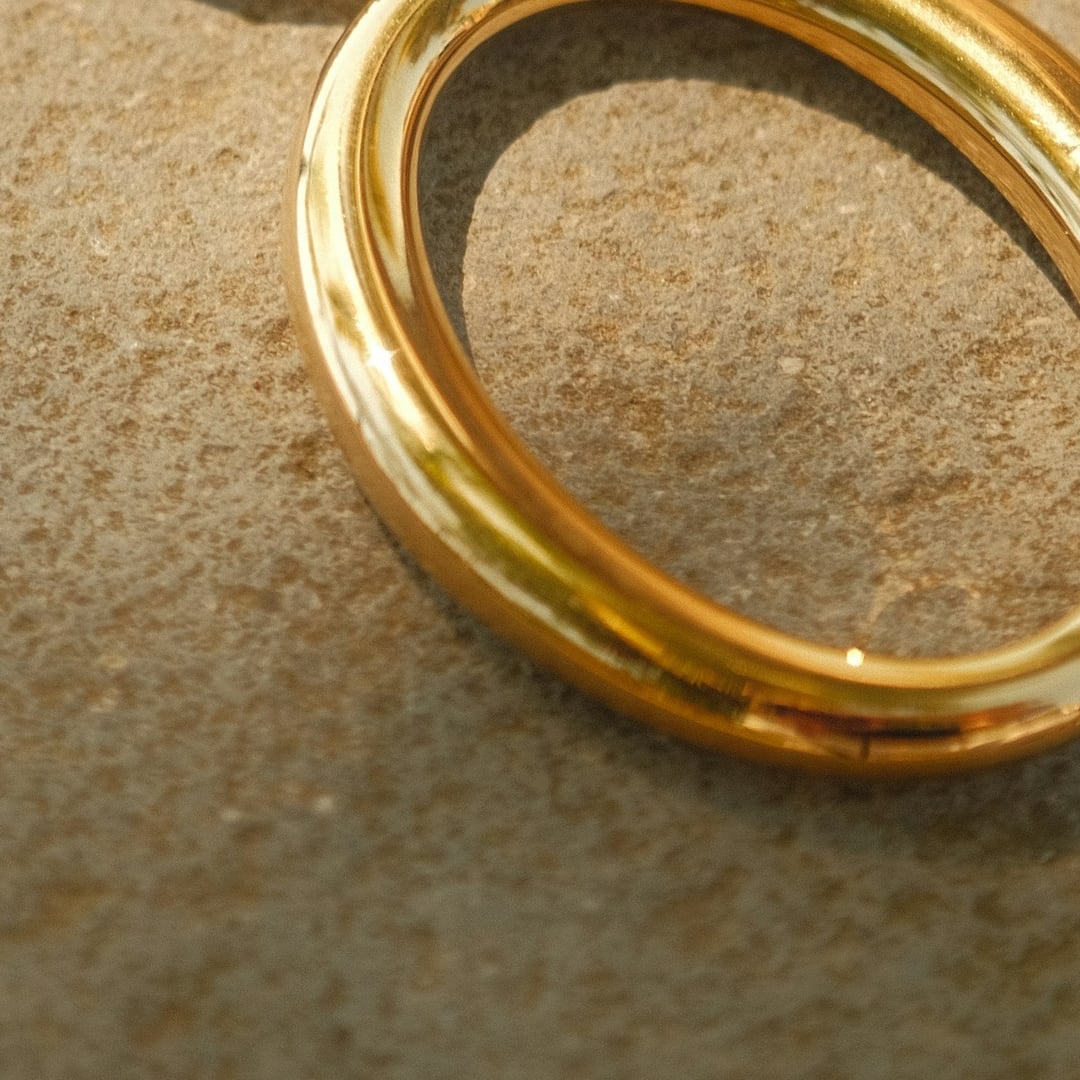 Close-up detail — gold snake chain necklace with an open oval pendant on textured stone