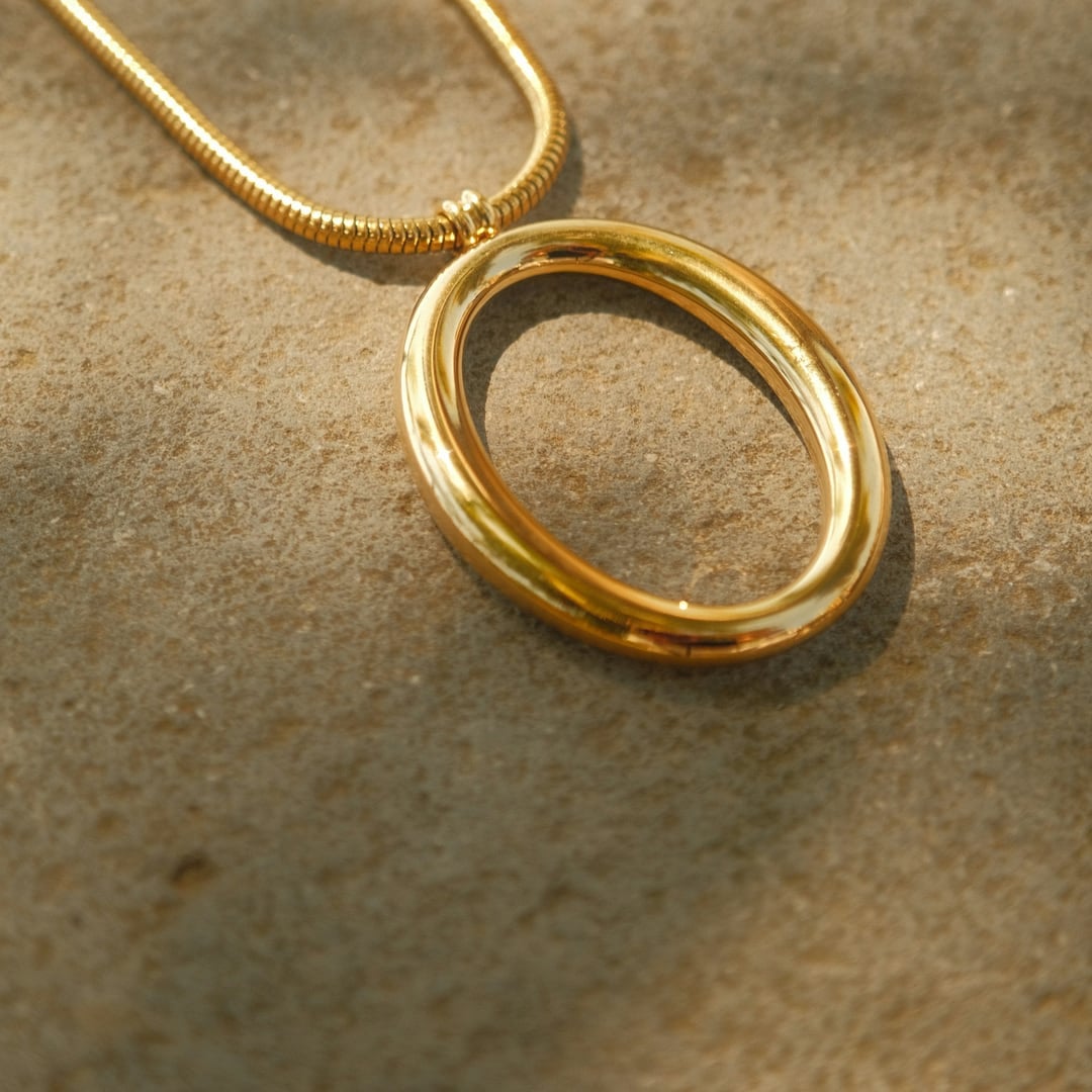 Gold snake chain necklace with an open oval pendant on textured stone