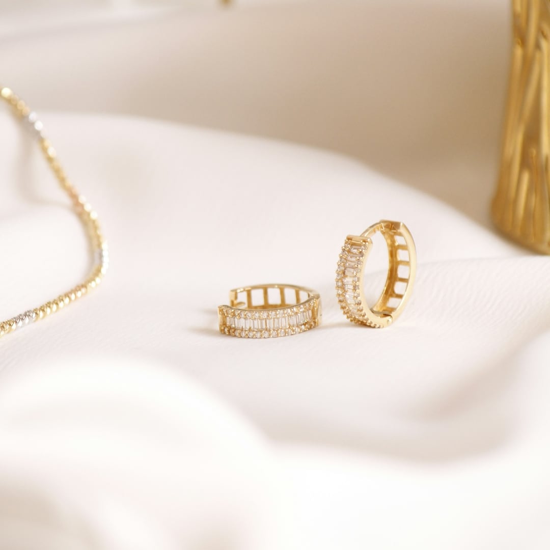 Gold huggie hoop earrings set with diamonds on ivory satin
