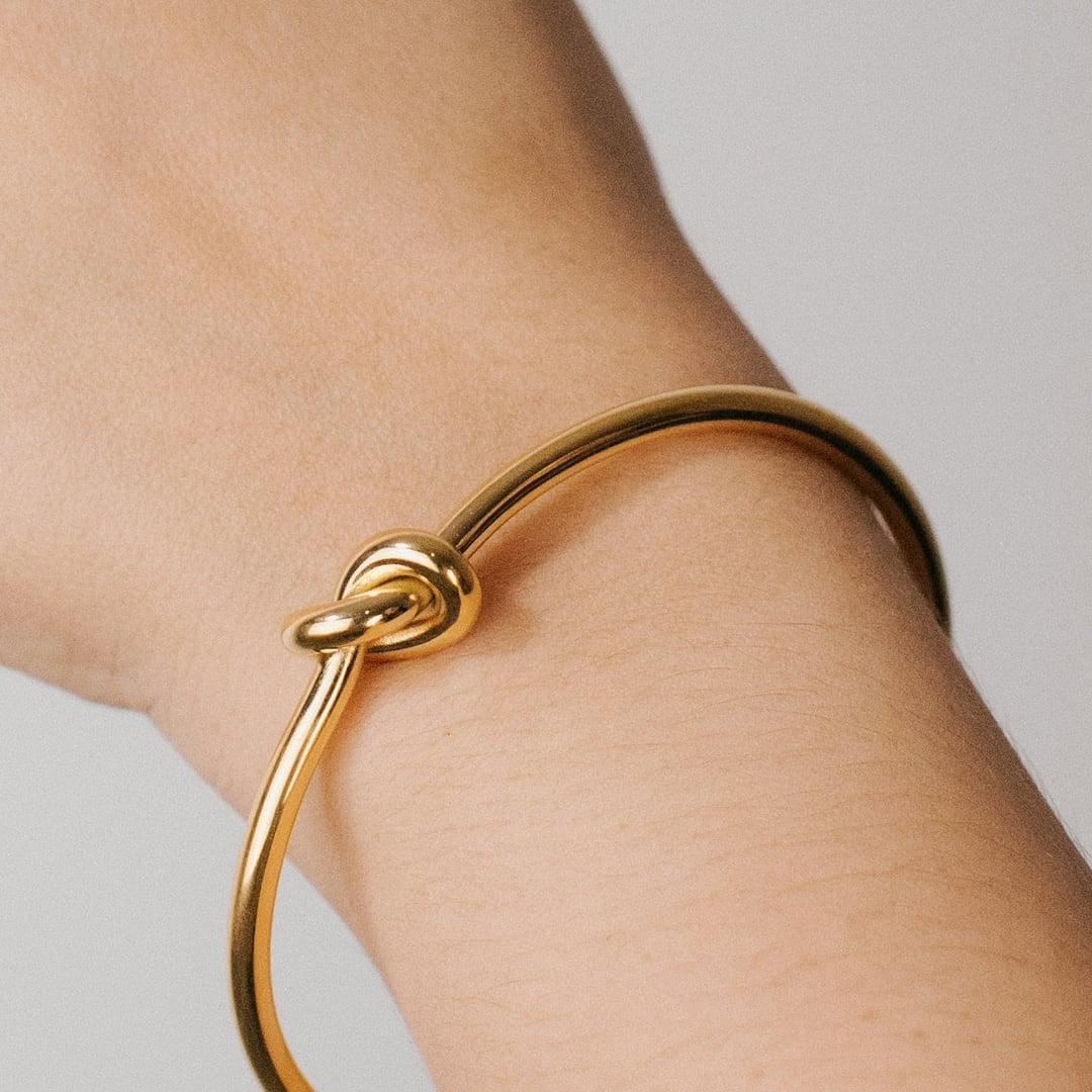 Close-up detail — slim open gold cuff bracelet worn on a raised wrist