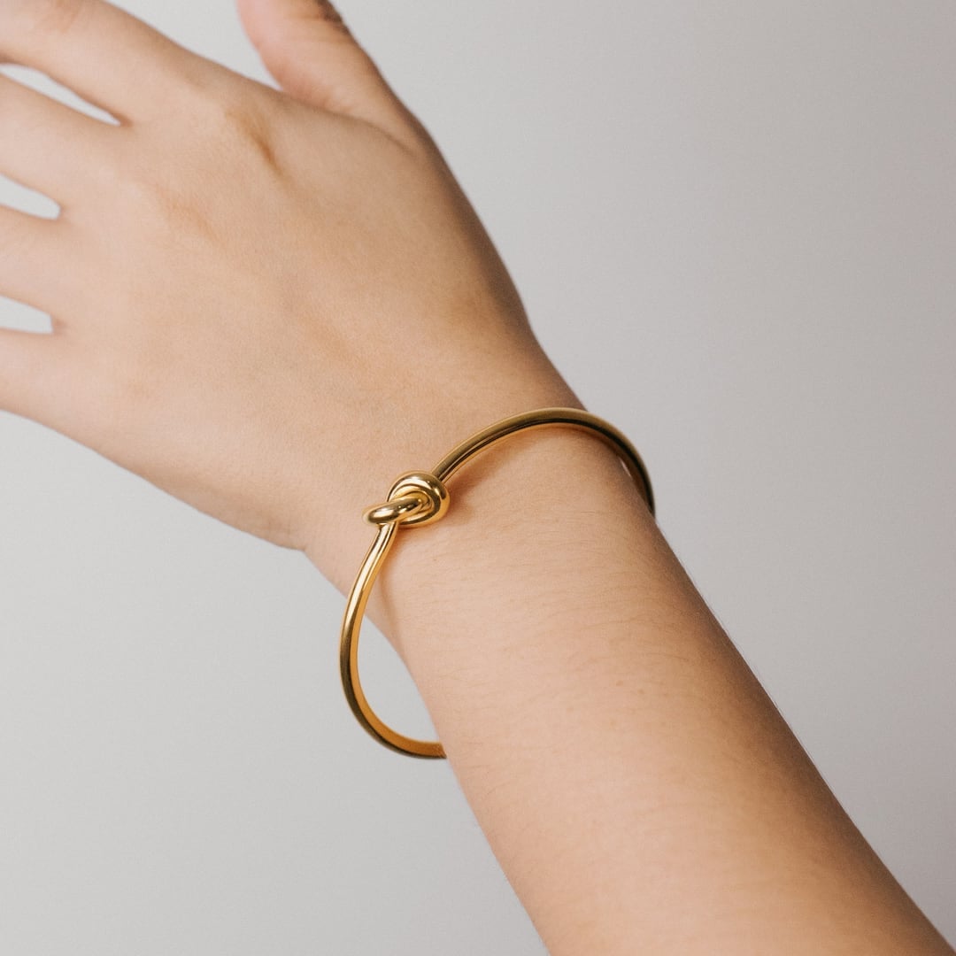 Slim open gold cuff bracelet worn on a raised wrist