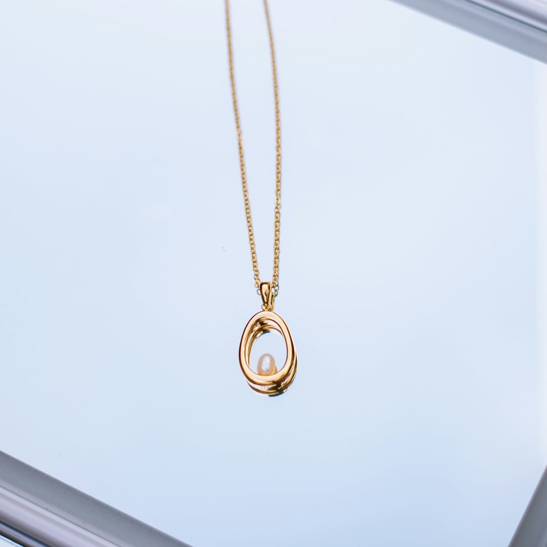 Fine gold necklace with a pearl drop pendant hanging against a pale window