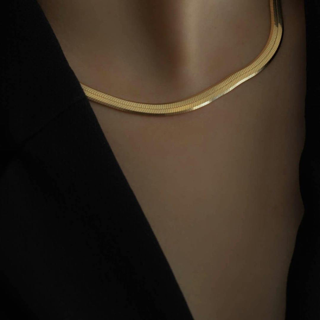 Close-up detail — woman in a black blazer wearing a flat gold herringbone collar necklace