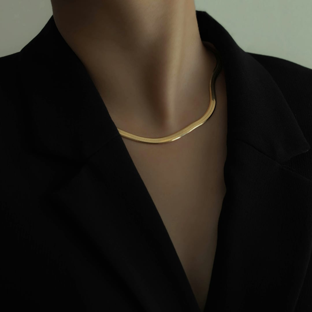 Woman in a black blazer wearing a flat gold herringbone collar necklace