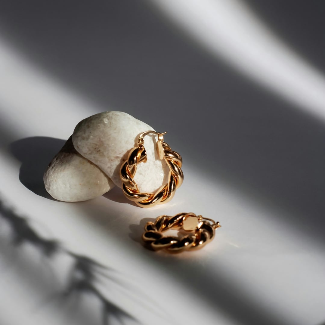 Twisted gold hoop earrings resting on white stones with long shadows